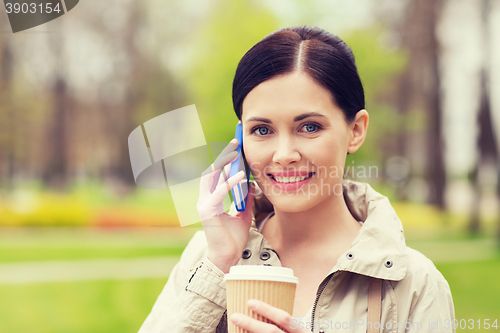 Image of smiling woman with smartphone and coffee in park