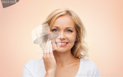 Image of smiling woman in white t-shirt touching her face