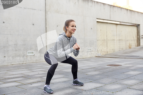 Image of happy woman doing squats and exercising outdoors
