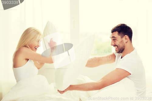 Image of happy couple having pillow fight in bed at home