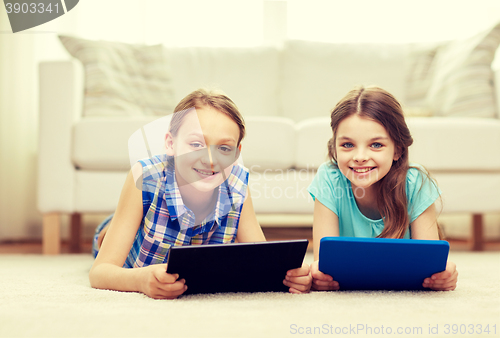 Image of happy girls with tablet pc lying on floor at home