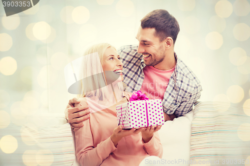 Image of happy man giving woman present over holiday lights