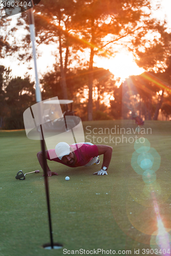 Image of golf player blowing ball in hole with sunset in background