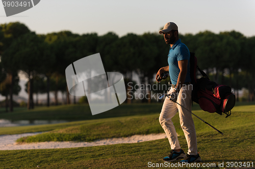 Image of golfer  walking and carrying golf  bag at beautiful sunset