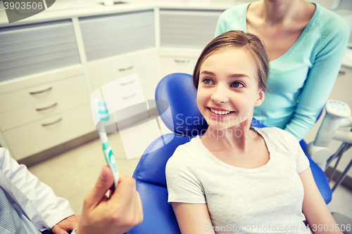 Image of happy dentist showing toothbrush to patient girl