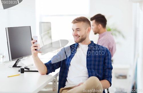 Image of happy creative man texting on cellphone at office