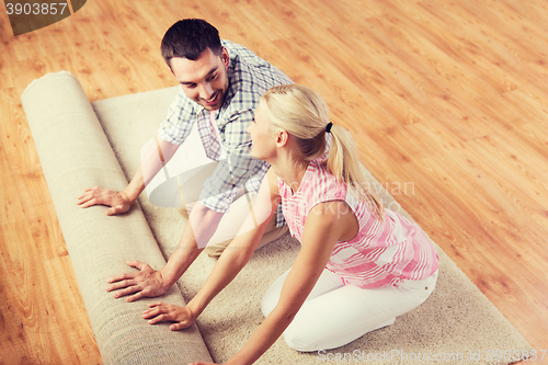 Image of happy couple unrolling carpet or rug at home