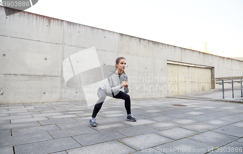 Image of happy woman doing squats and exercising outdoors