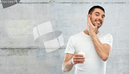 Image of happy young man applying cream or lotion to face