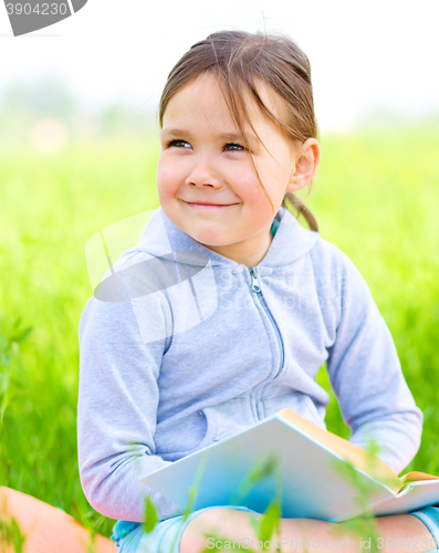 Image of Little girl is reading a book outdoors