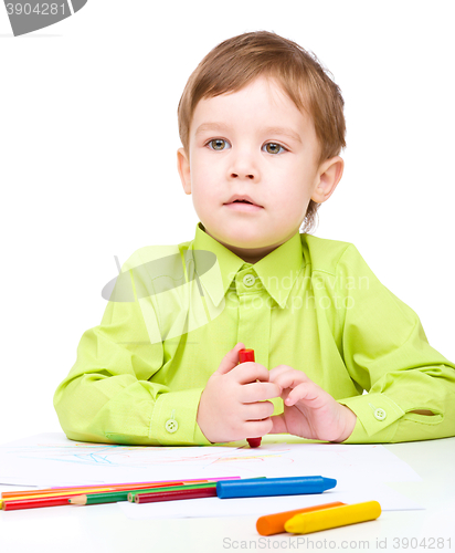 Image of Little boy is drawing on white paper using crayon