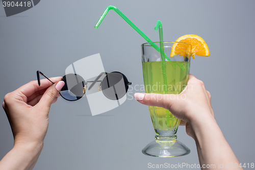 Image of The female hands with cocktail and sunglasses on gray background