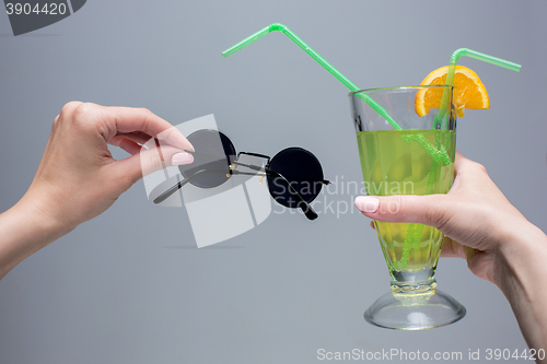 Image of The female hands with cocktail and sunglasses on gray background