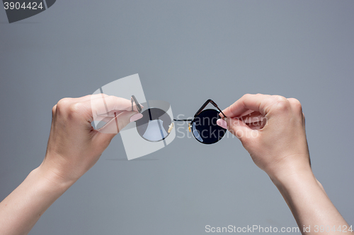 Image of The female hands holding sunglasses on gray background.