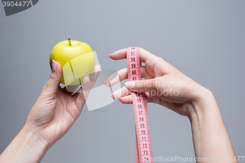 Image of Green apple in female hands on gray background. Weight loss, diet