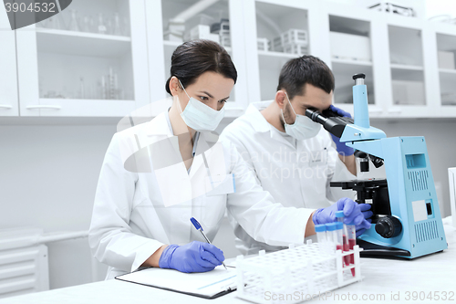 Image of scientists with clipboard and microscope in lab