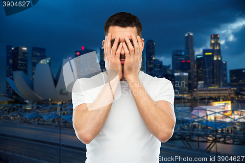 Image of man in white t-shirt covering his face with hands