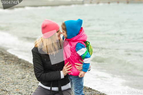 Image of Little girl and her mother touching noses on the beach in cold weather