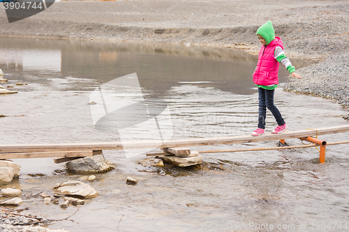 Image of Little girl cautiously goes on the board across the pond