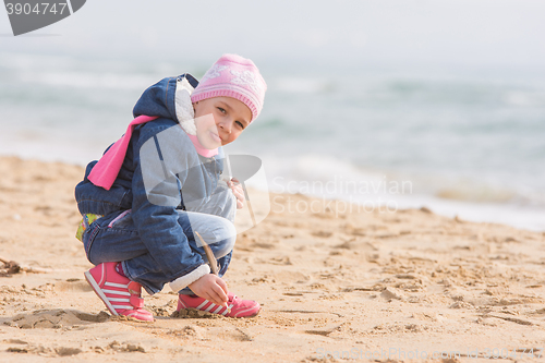 Image of Five-year girl in the spring of the pen draws on the sand by the sea, and has shown language in the frame