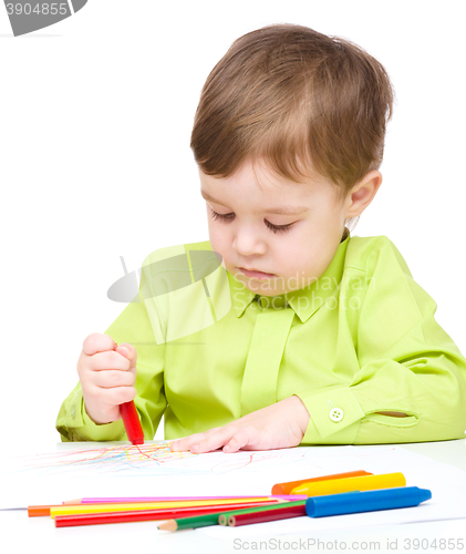 Image of Little boy is drawing on white paper using crayon