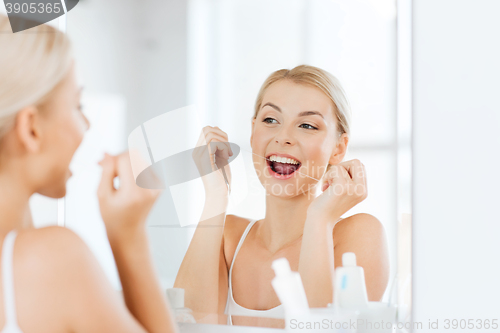 Image of woman with dental floss cleaning teeth at bathroom