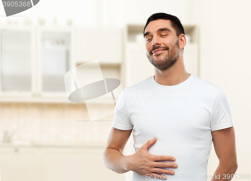 Image of happy full man touching tummy over kitchen