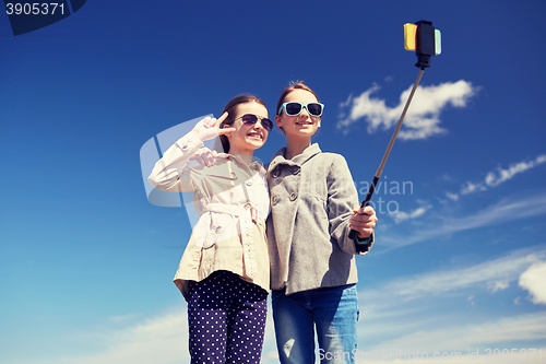 Image of happy girls with smartphone selfie stick