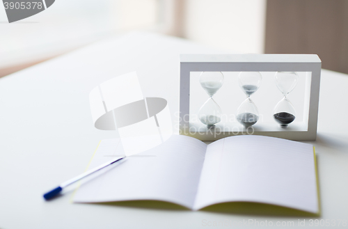 Image of close up of notebook, pen and hourglass on table