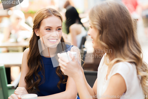 Image of smiling young women with coffee cups at cafe