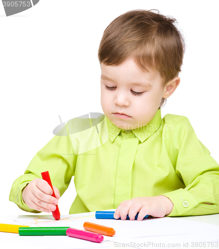 Image of Little boy is drawing on white paper using crayon