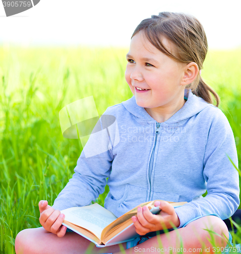 Image of Little girl is reading a book outdoors