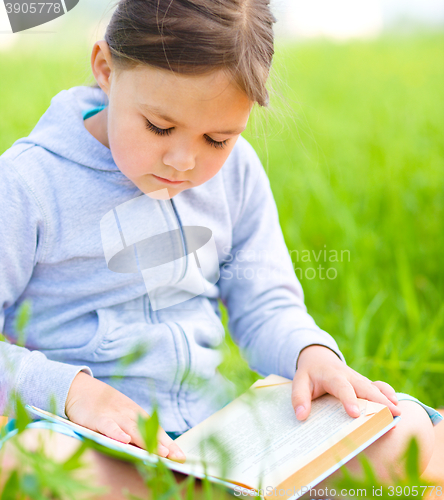 Image of Little girl is reading a book outdoors