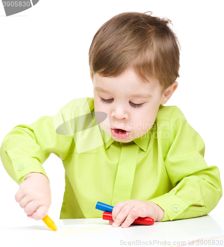 Image of Little boy is drawing on white paper using crayon
