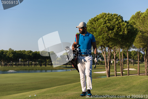Image of golfer  walking and carrying bag