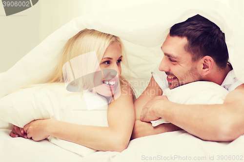 Image of happy couple lying in bed and talking at home