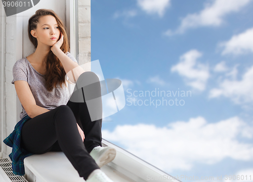 Image of sad pretty teenage girl sitting on windowsill