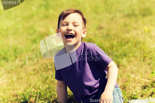 Image of happy little boy sitting on grass outdoors