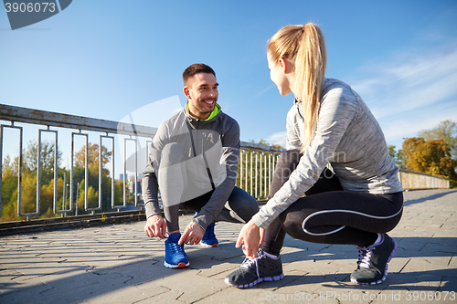 Image of smiling couple tying shoelaces outdoors