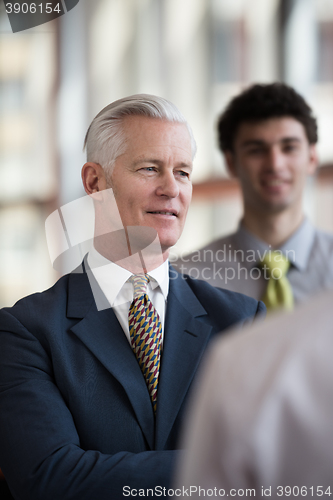 Image of portrait of senior businessman as leader  with staff in backgrou