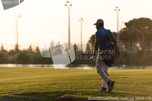 Image of golfer  walking and carrying golf  bag at beautiful sunset