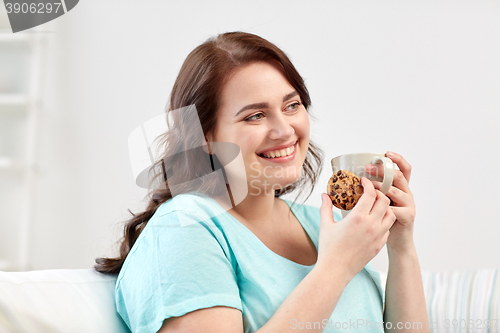 Image of happy plus size woman with cup and cookie at home