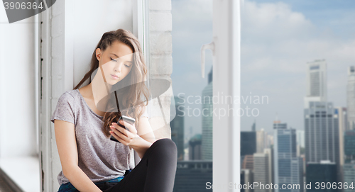 Image of sad pretty teenage girl with smartphone texting