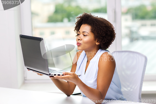 Image of african woman sending kiss to laptop computer