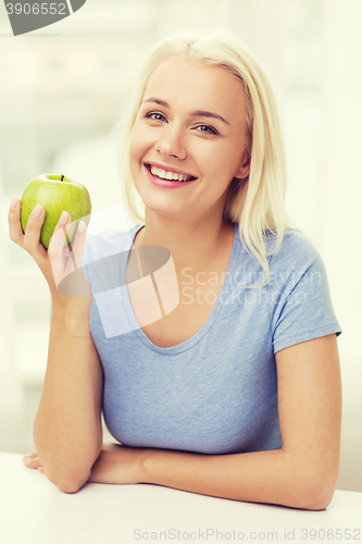 Image of happy woman eating green apple at home