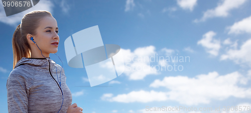 Image of happy woman with earphones running over blue sky