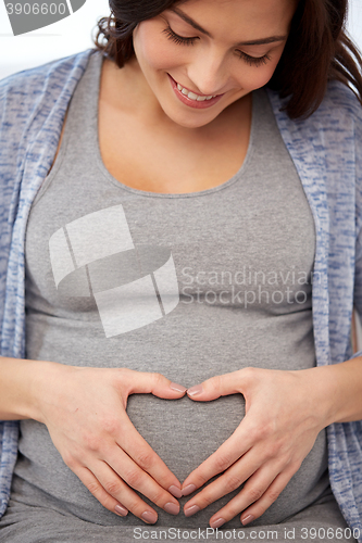 Image of happy pregnant woman making heart gesture at home