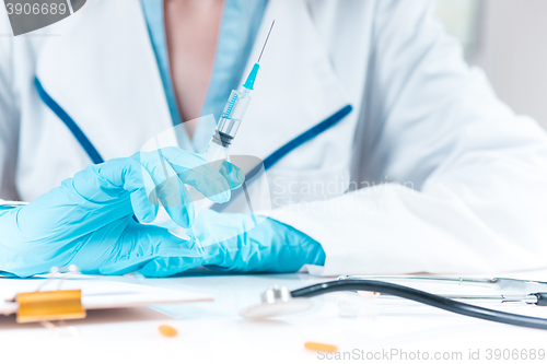 Image of The hand in blue glove holding syringe against white medical gown 