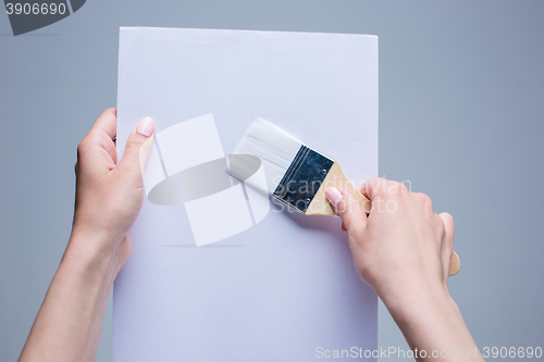 Image of Hands holding painting brush on white canvas