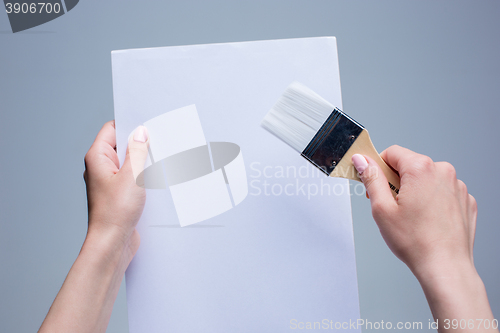 Image of Hands holding painting brush on white canvas